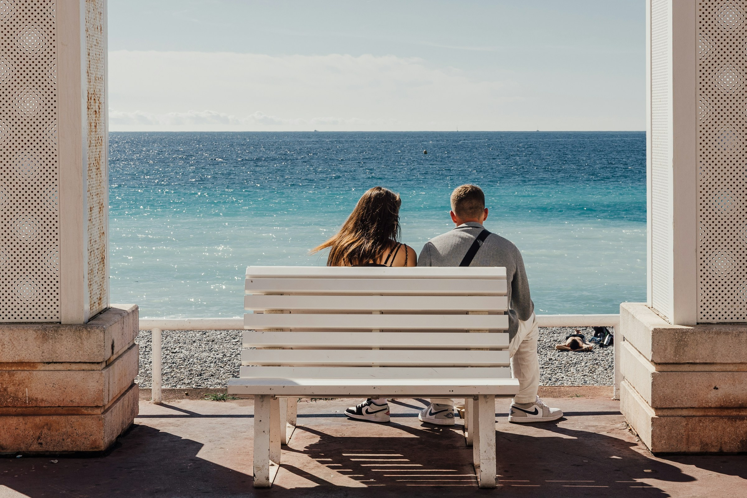 A couple sits on a white bench looking out at the beautiful Ocean