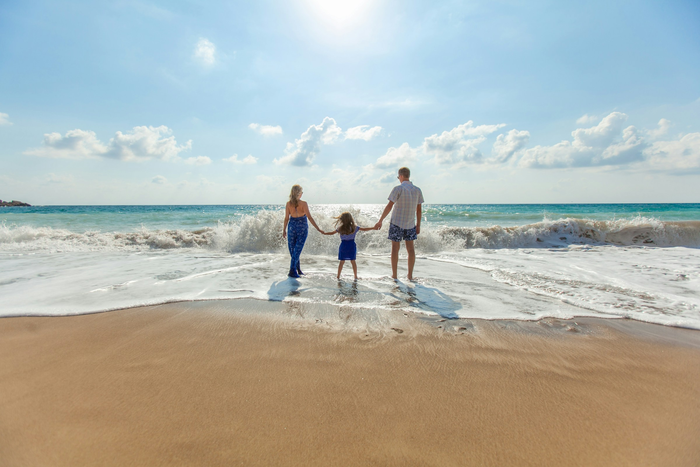A mother and father holding their daughters hands standing in the ocean.