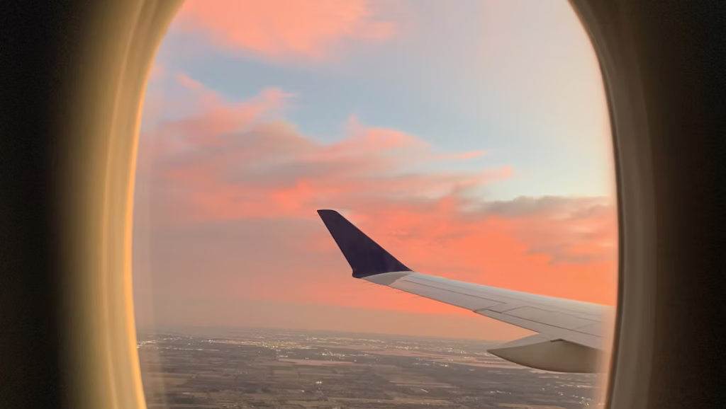 Airplane wing view at sunset through a window with pink and orange skies during flight
