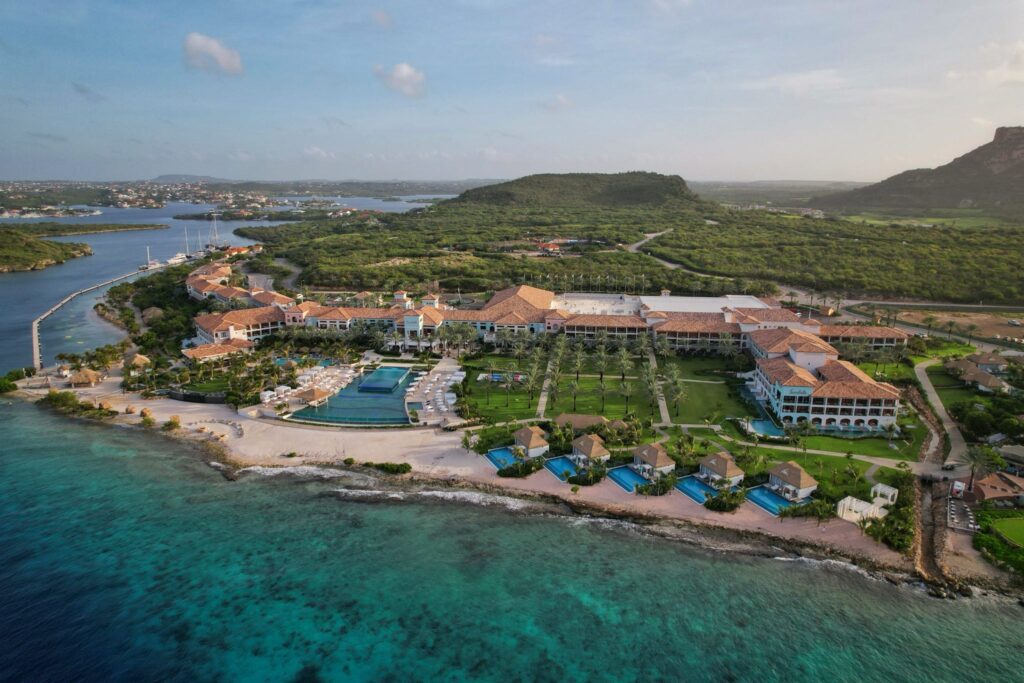 Aerial view of Sandals Royal Curaçao resort along the Caribbean coastline with oceanfront pools and lush island scenery