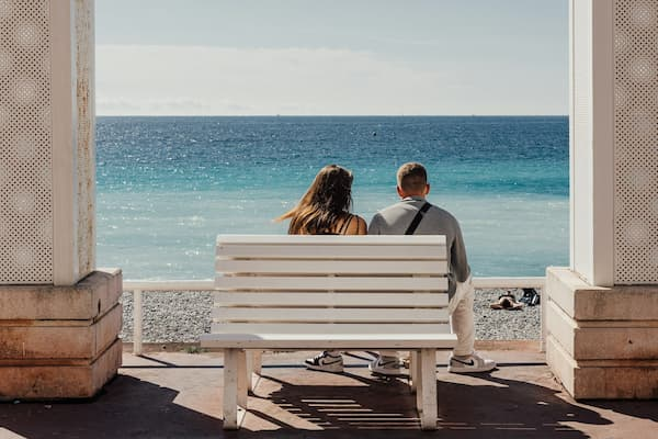 A couple sits on a white bench looking out at the beautiful Ocean